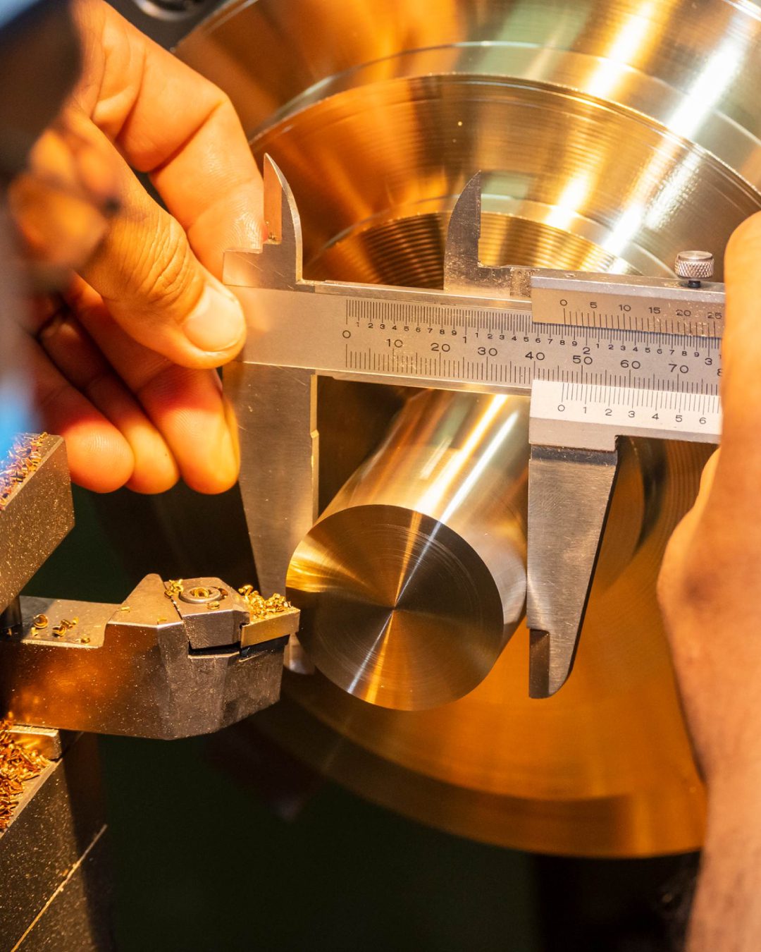 Metal cylinder measurement with caliper on lathe.